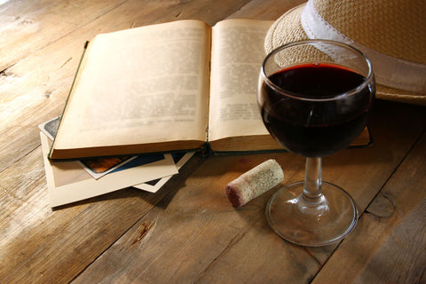 glass of red wine next to open book and cork